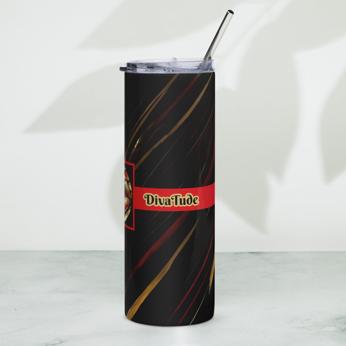 Left of a black stainless-steel tumbler with black and gold word 'DivaTude' on a red line and a black patterned background