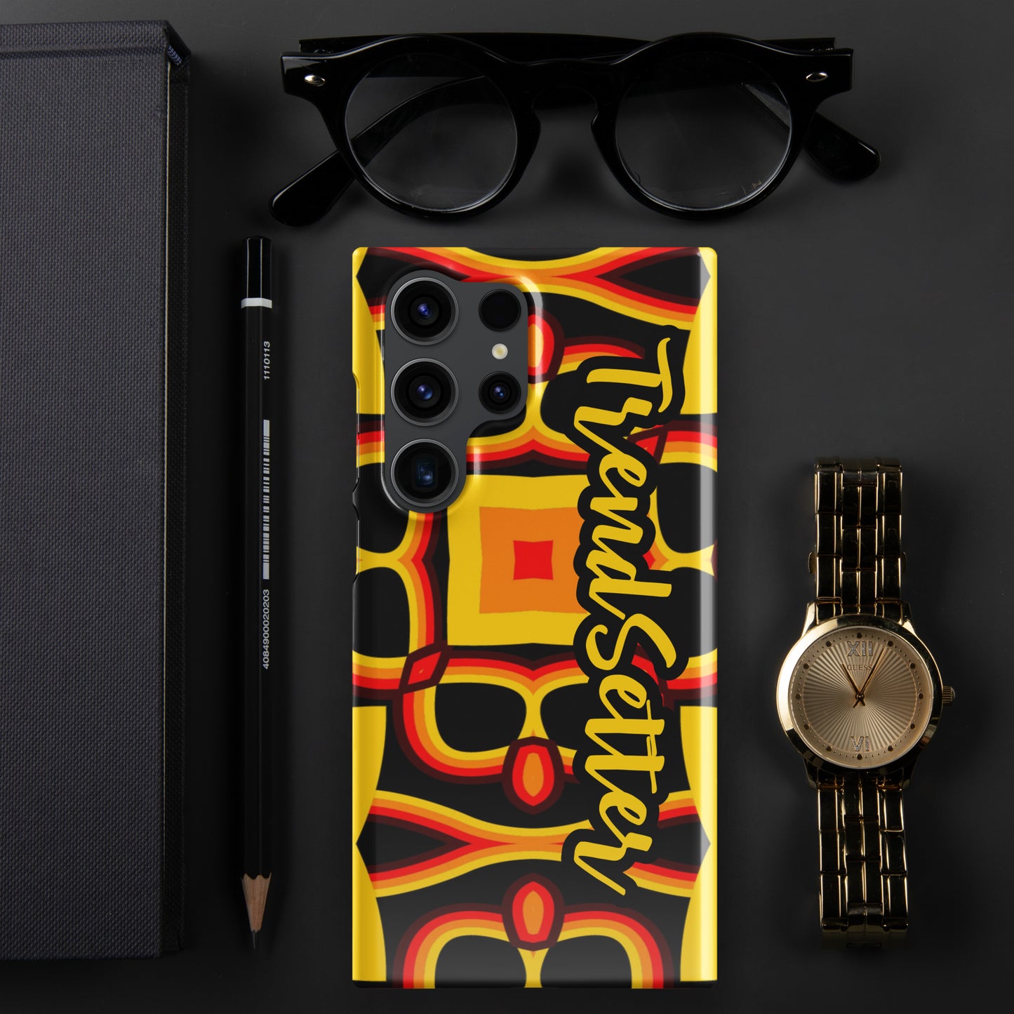 Front of gold, yellow, red and black print Samsung s23 glossy case with text "TrendSetter' in black and gold
