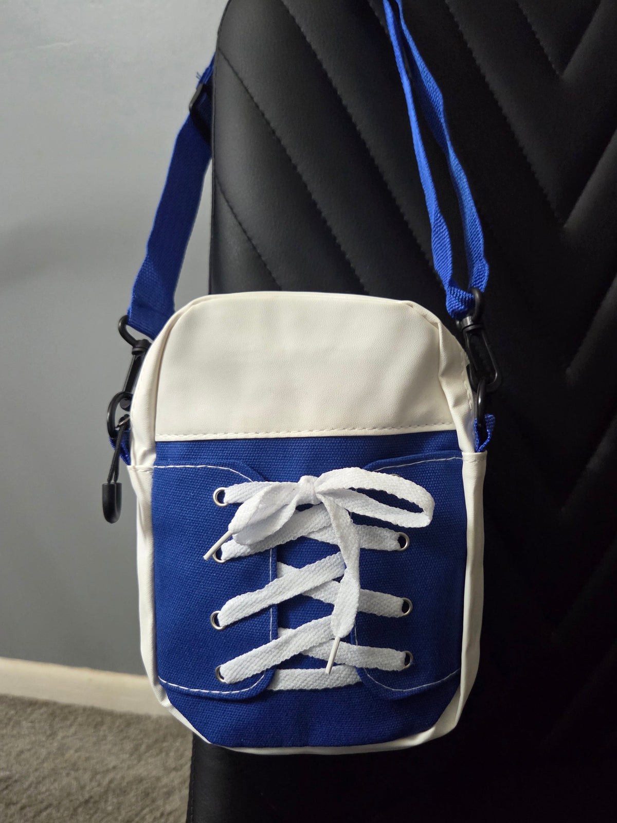 Back view of Blue and White Sneaker cross body bag in faux leather and cloth blend fabrics, featuring a blue strap, resting on a black leather chair. Close up view.