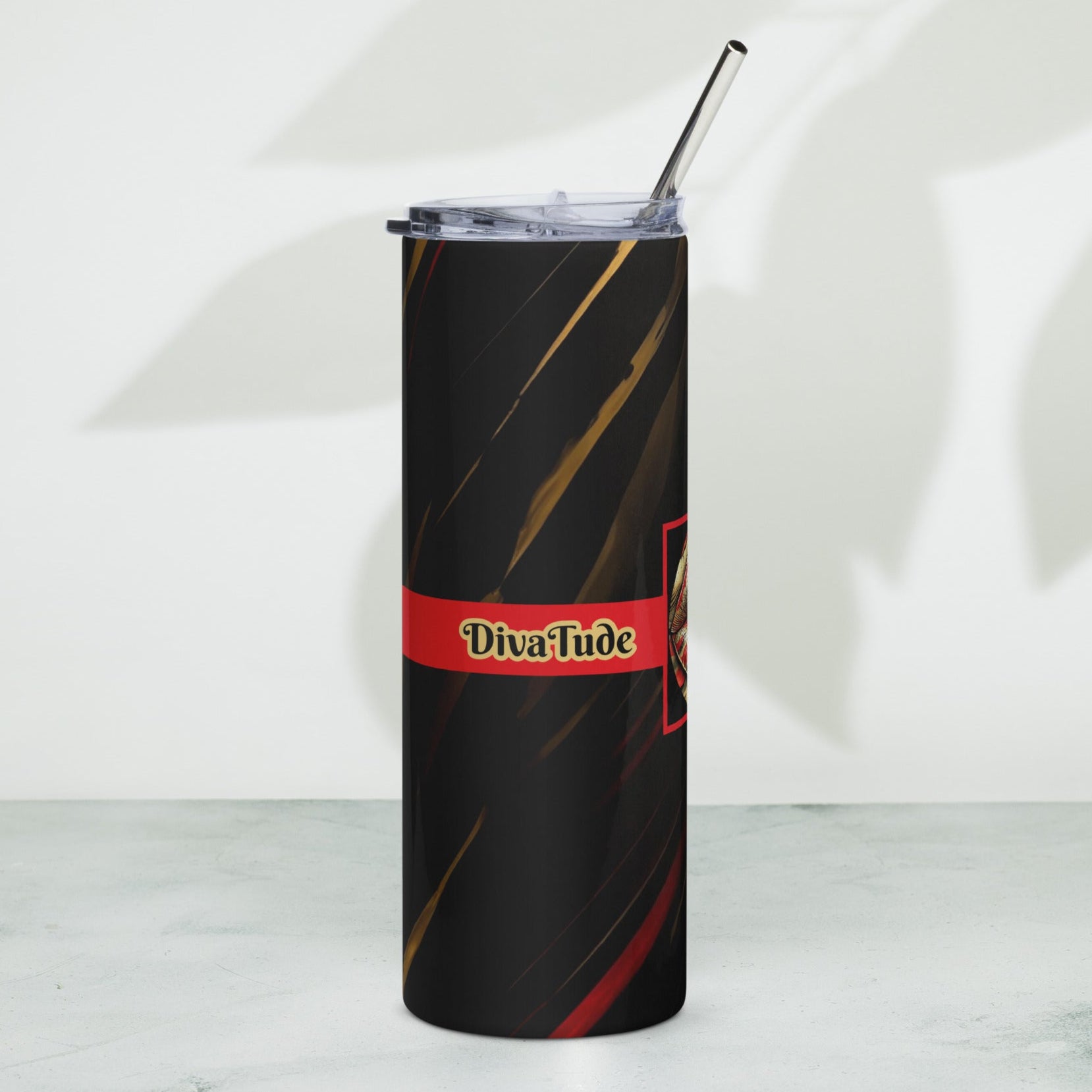 Right of a black stainless-steel tumbler with black and gold word 'DivaTude' on a red line and a black patterned background