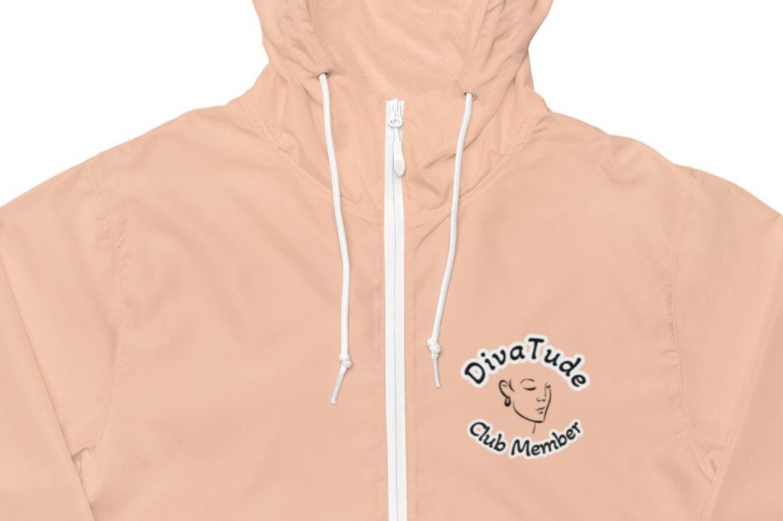 Front of women's blush windbreaker with image on top left of embroidered lady's face in black with grey and black text saying "DivaTude' above and 'Club Member' below 