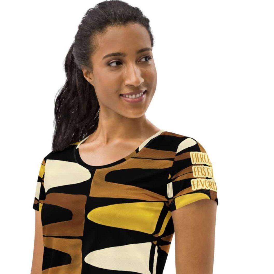 Left angled view of a woman wearing black, brown, beige and gold print t-shirt with gold and white text saying 'Fierce.Feisty.Favored.' on left sleeve