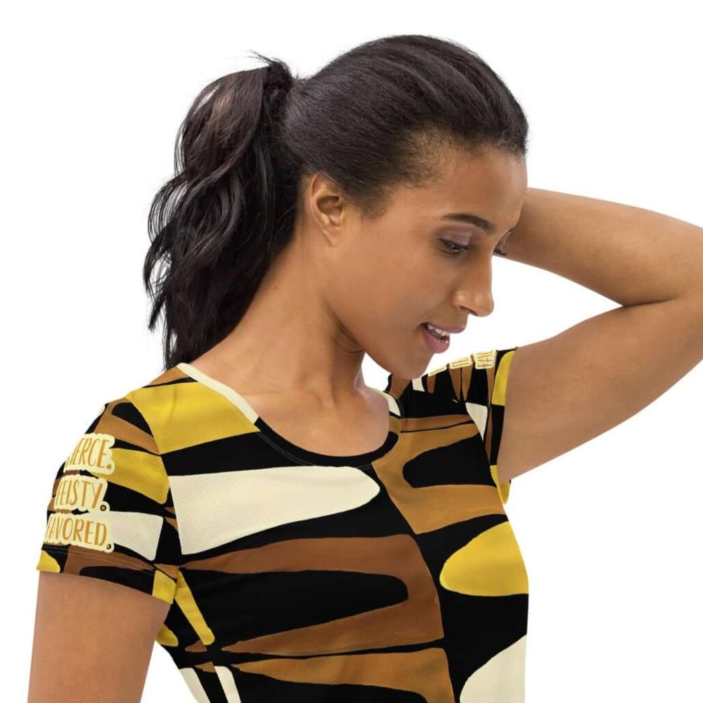 Right angled view of a woman wearing black, brown, beige and gold print t-shirt with gold and white text saying 'Fierce.Feisty.Favored.' on right sleeve