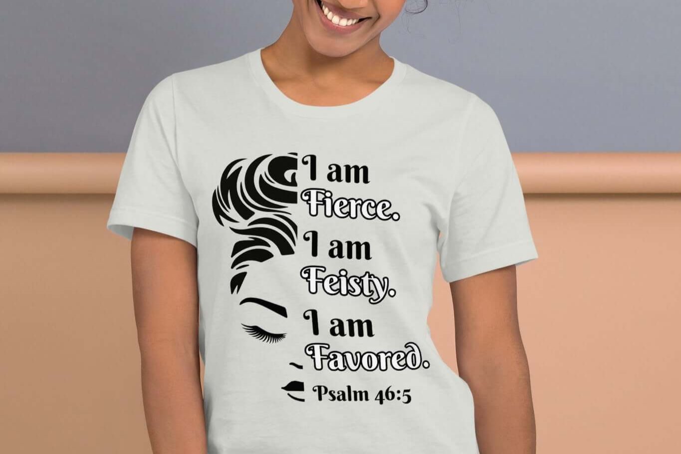 Front of silver t-shirt with image of half woman's face with black and white text saying "I am fierce, I am feisty, I am favored and Psalm 46:3'