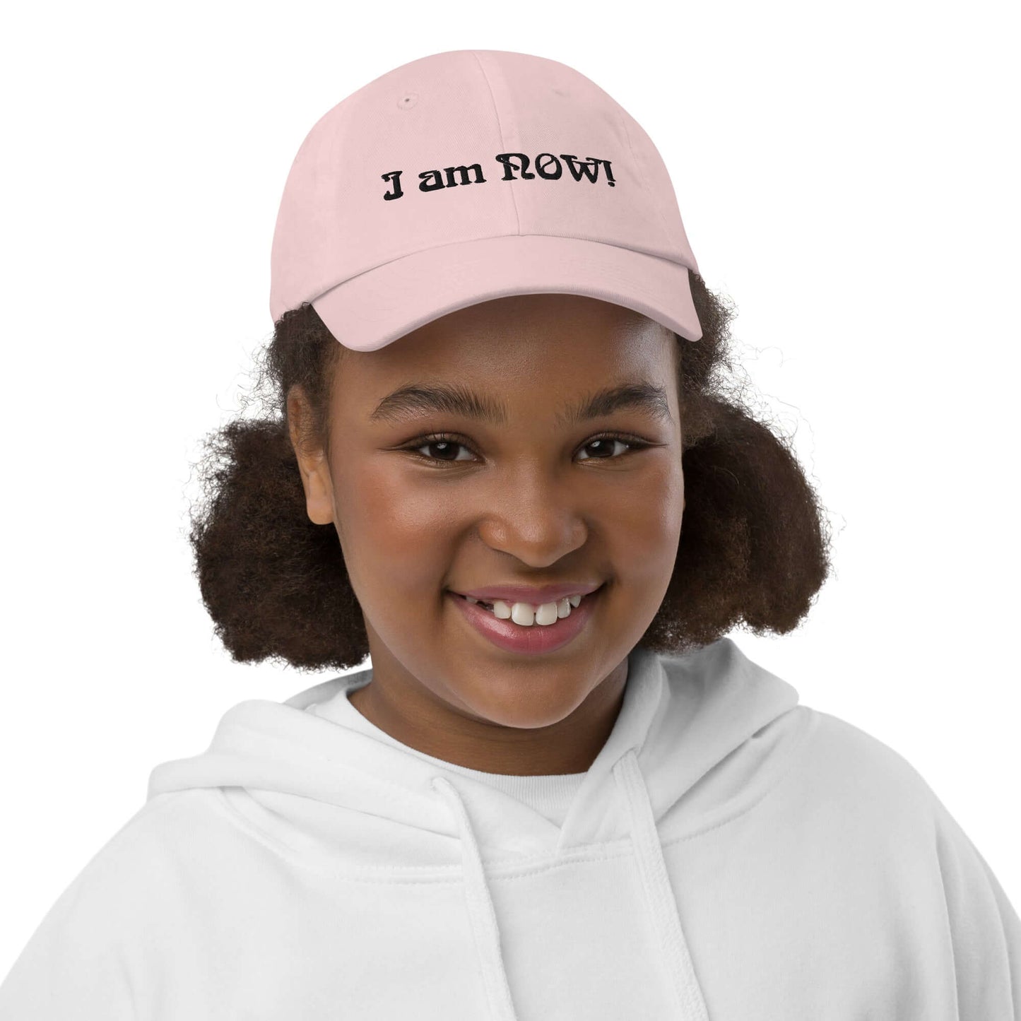 Front view of youth wearing a light pink baseball cap with text saying 'I am now' across the front