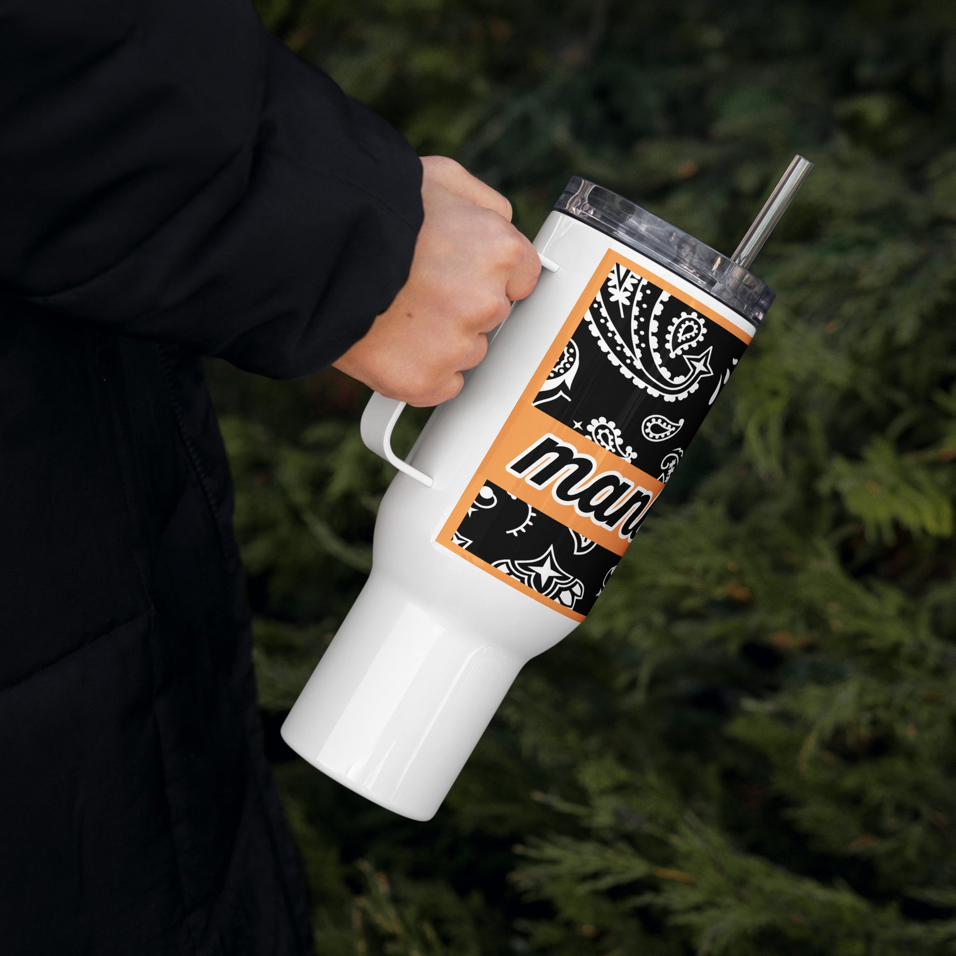 Right of travel mug with black and white paisley and word 'manly' on top of orange banner being held