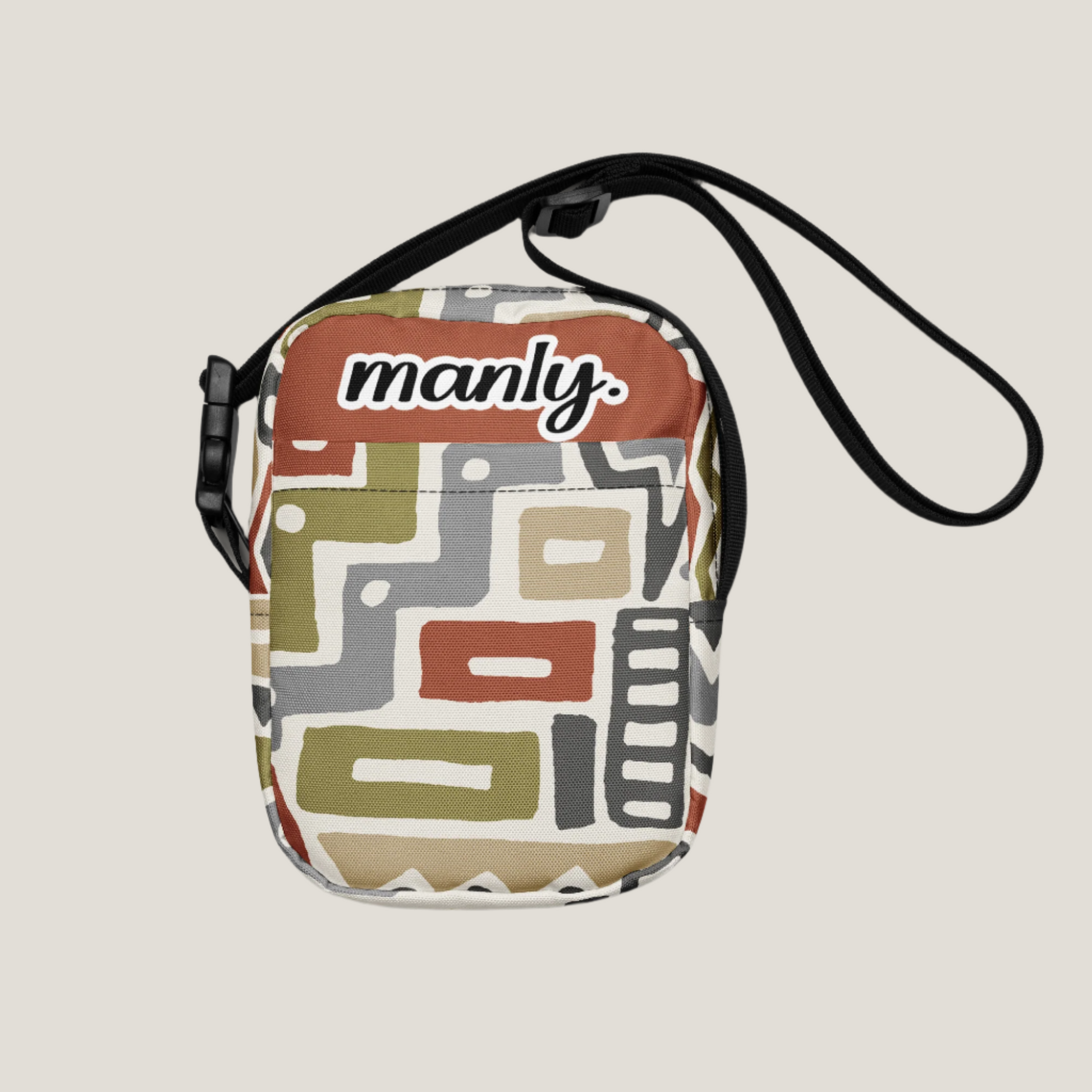 Front view of Manly Tribal Tune Utility Crossbody Bag in beige and tan print text "manly" at top