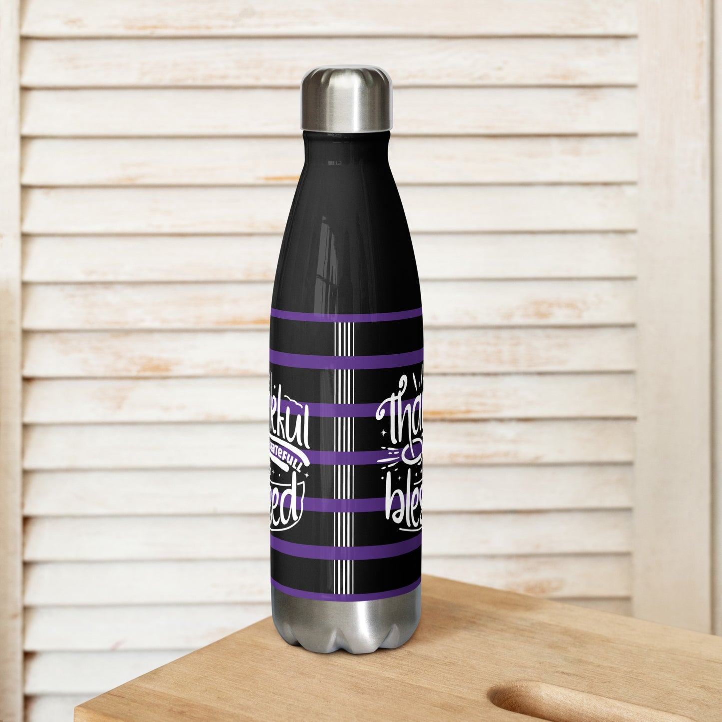 Left side of a black 17 oz stainless steel water bottle with purple and white lines and white text saying 'Thankful and blessed'