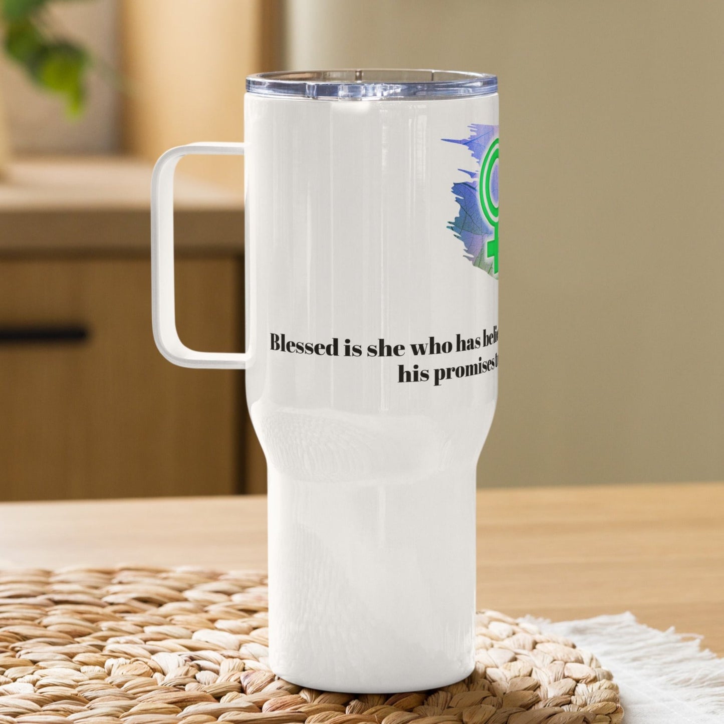 Left view of a white travel mug with partial view of the green, white, and black image representing woman of God and black text from Luke 1:45 underneath