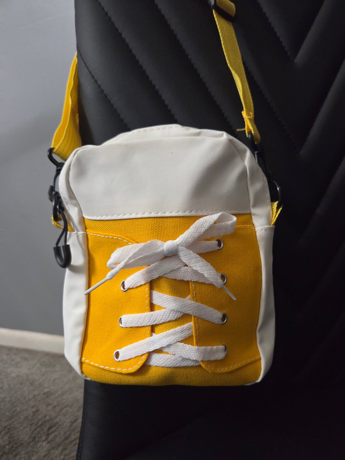 Back view of Yellow and White Sneaker cross body in faux leather and cloth blend fabrics, featuring a yellow strap, resting on a black leather chair. Close up view.